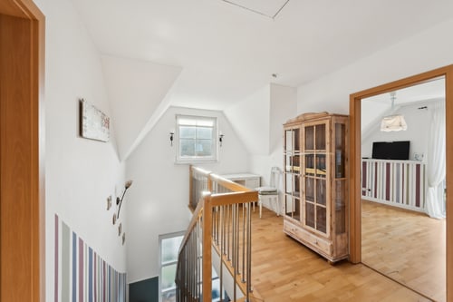 Flur im Dachgeschoss mit Holztreppe, Dachfenster, Holzboden und offenem Durchgang zu einem Zimmer.