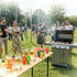 Menschen grillen im Freien auf einem Rasenfeld mit einem Tisch voller Getränke.