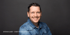 Stefan Kjaer, Chief People Officer, lächelt in einer Jeansjacke vor grauem Hintergrund.