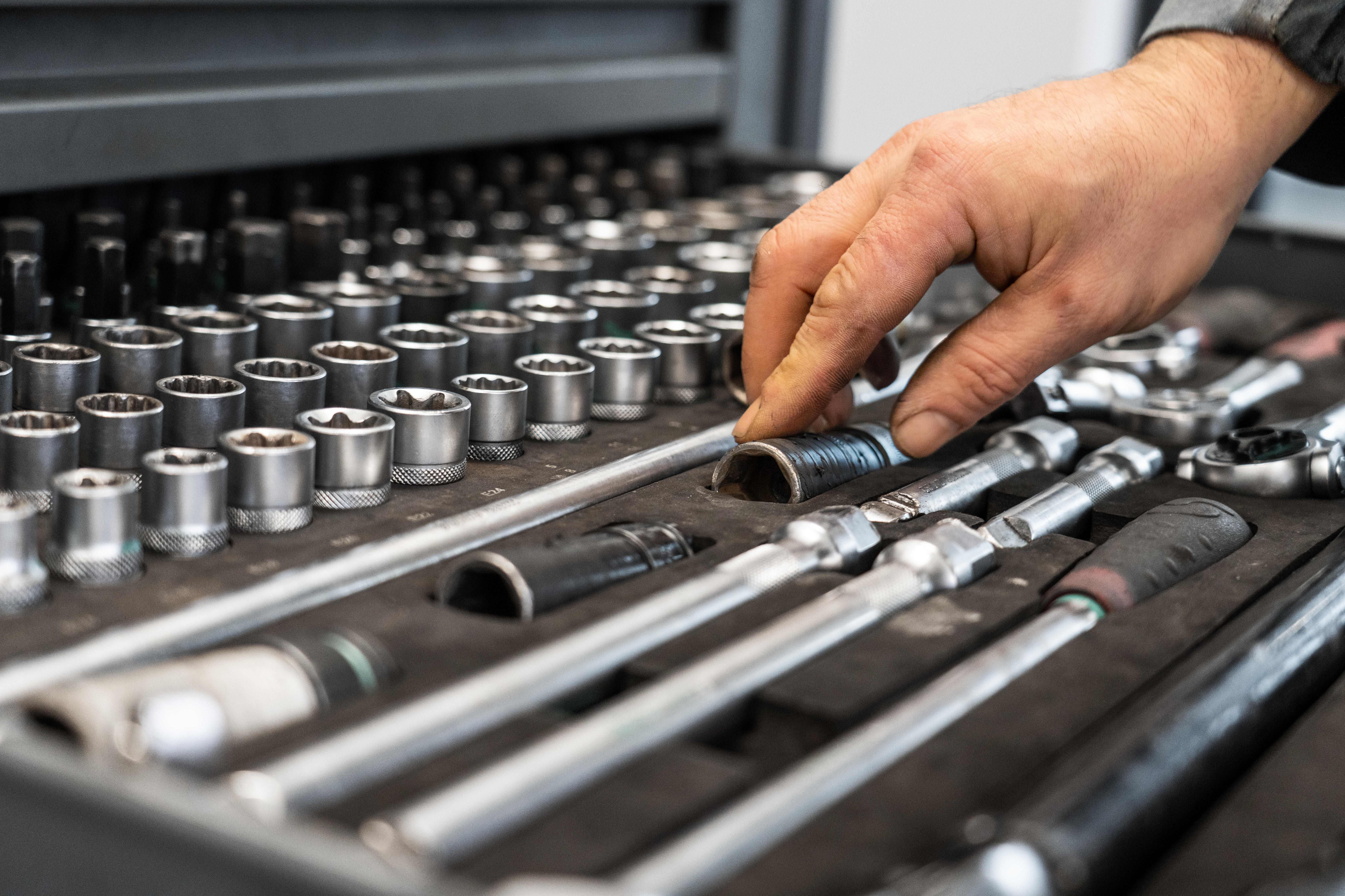 Eine Hand greift in einen Werkzeugkasten mit verschiedenen Stecknüssen und Schraubenschlüsseln.