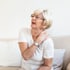 A senior woman in glasses holds her painful shoulder, grimacing in discomfort.