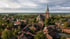 Luftaufnahme einer Kleinstadt mit Backsteinhäusern, einer großen Kirche mit grünem Turm und umliegenden grünen Feldern. Bild von Ochtrup