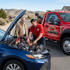 Towing Sandy jump start service assisting a driver by connecting jumper cables to a vehicle with a dead battery on a residential roadway.