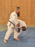 Ein Mann in einem weißen Judoanzug mit schwarzem Gürtel trainiert mit einem anderen Mann auf blauen Matten.
