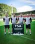 Vier Männer in Sportbekleidung halten ein Schild mit der Aufschrift "TSA TorwartSchule Allmendinger am Weserstadion".