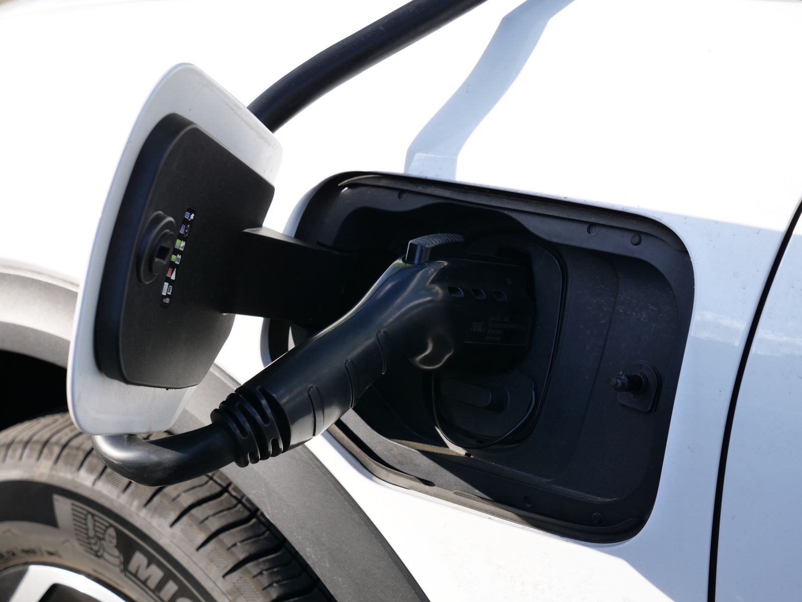 EV charging connector plugged into a vehicle in sunlight