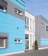 Modern multi-story commercial building with light blue, gray, and white paneled exterior walls under a clear sky.