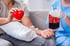 Person receiving UVBI therapy, holding a red heart, with a nurse holding a blood bag.
