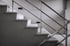 Graue Betontreppe mit Metallgeländer und zwei schwarzen Wandleuchten an heller Wand.