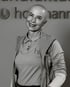 Glückliche, kahlköpfige Frau in Poloshirt und Weste lächelt vor einem Hoffmann-Logo.