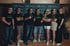 Sieben Personen in schwarzen T-Shirts und grünen Sonnenbrillen posieren vor einer Christian Bernhausen Logo-Wand.