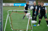 Vier Jungen in Sportkleidung mit Torwarthandschuhen und Fußbällen trainieren auf einem Fußballfeld.