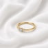 Goldener Ring mit drei kleinen Diamanten auf gewelltem weißem Stoff.