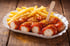 Currywurst mit Pommes Frites und Holzgabel in weißer Pappschale auf rustikalem Holztisch.