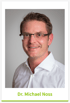 Porträt von Dr. Michael Noss mit Brille und weißem Hemd vor grauem Hintergrund.