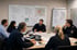 Polizeibeamte und Zivilpersonen bei einer Lagebesprechung im Büro vor einem Whiteboard mit Karten und Notizen - Software für Alarm- und Gefahrenabwehrplanung - Notfall- und Krisenmanager (NKM®).