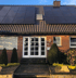 Dunkle Solarmodule auf einem Ziegeldach eines roten Backsteinhauses mit weißer Doppeltür.
