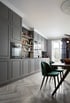 Graue Einbauküche mit Backofen, Spüle und offenen Regalen. Daneben Esstisch mit zwei teal-farbenen Stühlen.