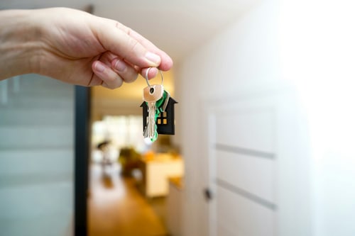 Hand hält einen Hausschlüssel vor einer Haustür