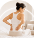 Woman sitting on a bed holding her lower back in pain.