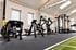 Moderner Fitnessraum mit schwarzen Kraftgeräten, einem Power-Rack, Laufband und grünem Kunstrasenstreifen auf dunklem Boden.