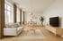 Heller, minimalistischer Wohn- und Essbereich mit beige Sofa, Holztisch, TV-Schrank, Pflanze und großen Fenstern.