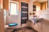 Modernes Badezimmer mit weißen Fliesen, Toilette mit blauem Sitz, Waschbecken, Spiegel und Handtuchheizkörper.
