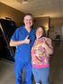 A woman in a floral dress smiling with a man in scrubs.

