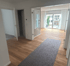 Leerer Flur mit Holzboden und grauem Läufer, der zu einem offenen Wohnbereich mit Fenstertüren führt.