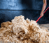 Hand mit rotem Stiel schiebt einen Haufen heller Holzspäne auf dunklem Hintergrund.