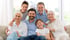 Drei Generationen einer lächelnden Familie sitzen zusammen auf einem hellen Sofa in einem lichtdurchfluteten Wohnzimmer.