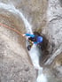 Person in Neoprenanzug seilt sich an orangefarbenem Seil neben einem Wasserfall in einer Schlucht ab.
