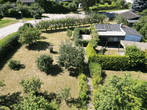 Luftaufnahme eines Hauses mit Garten, Bäumen und einer Straße.