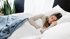 Eine Frau mit langen Haaren schläft ruhig in einem weißen Bett mit einer blauen Decke.