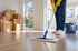 Reinigungskraft mit gelben Handschuhen wischt einen hellen Laminatboden in einer Wohnung mit Umzugskartons.