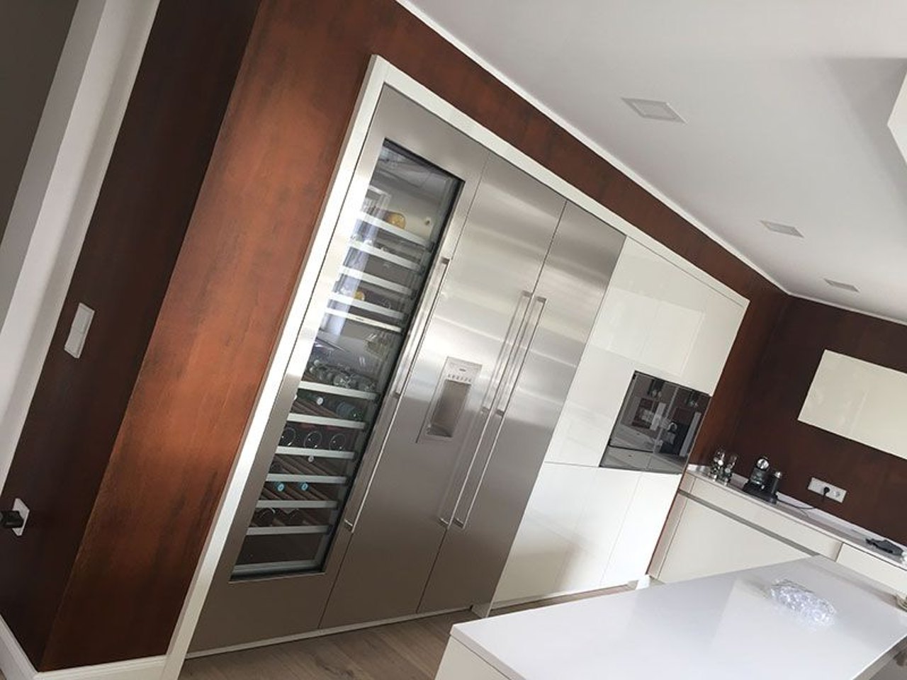 Moderne Küche mit eingebautem Weinkühlschrank und Edelstahl-Kühlschrank in einer dunklen Holzwand.