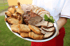 Servierplatte mit gebratenen Hähnchenkeulen, Schnitzeln, Schweinebraten und Rollbraten auf einer silbernen Platte.