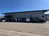 Modernes Gewerbegebäude mit Flachdach, davor parkenden Firmenwagen und Autos bei blauem Himmel.