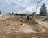Baugrube mit Aushub, Bagger, Betonpumpe, zwei Bauarbeitern und frisch gegossenem Fundament.