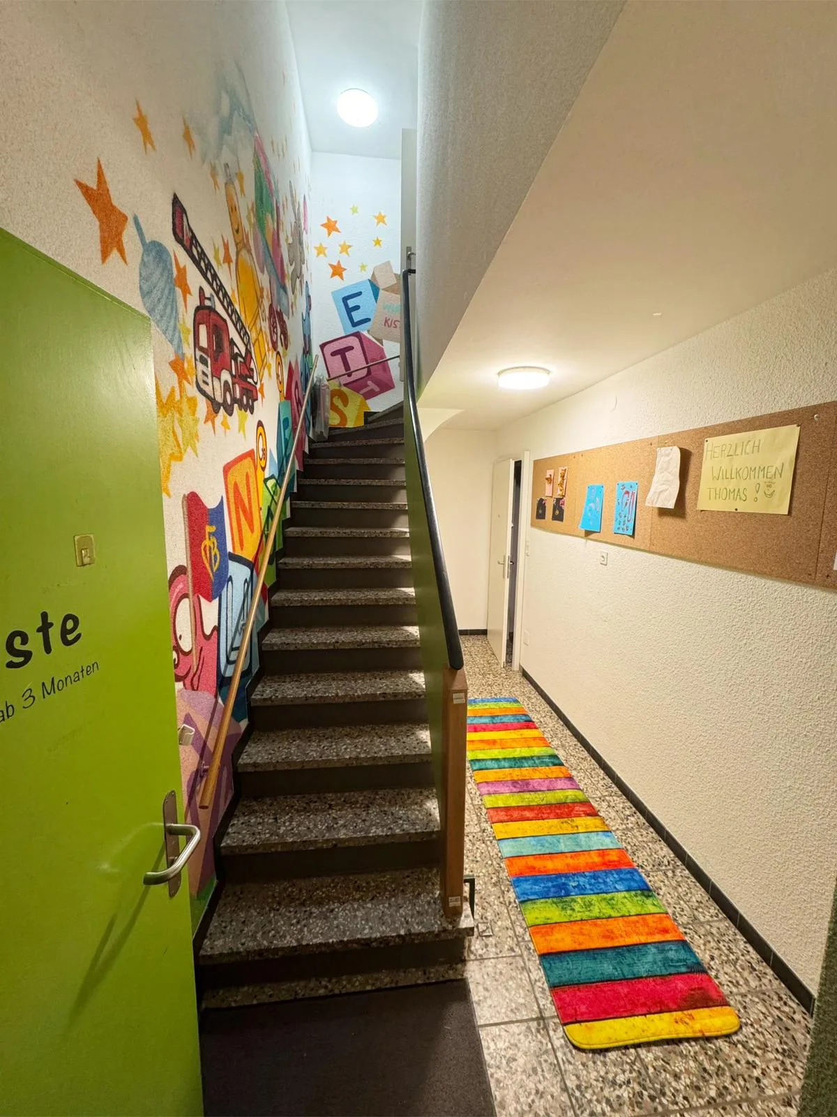 Treppenhaus der Kita mit bunter Graffitiwand und Regenbogen-Läufer.