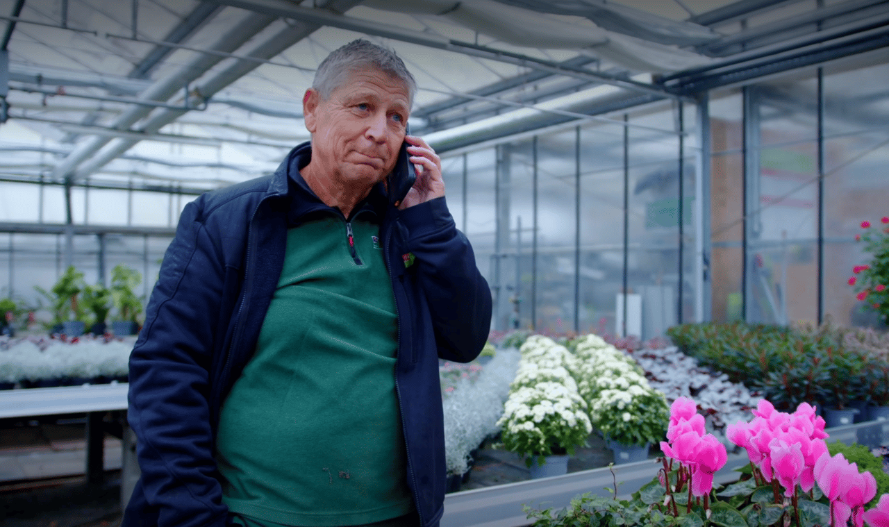 Friedhelm Fink telefoniert im Gewächshaus zwischen Blumen