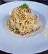 Spaghetti Carbonara mit Petersilie garniert auf einem weißen Teller, umgeben von geriebenem Parmesan.
