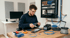 Ein Techniker arbeitet mit einer Crimpzange an Kabeln vor einem Netzwerkschrank mit Router und Patchpanel.