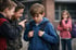 Ein trauriger Junge mit Rucksack wird von zwei Jungen verspottet, während ein Mädchen im Hintergrund zuschaut.