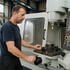 Ein Mann in dunkler Kleidung bedient eine CNC-Maschine in einer Werkstatt.