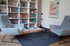 Zwei graue Sessel stehen sich in einem Raum mit einem Bücherregal, einem kleinen Tisch und einem Teppich gegenüber.