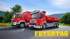 Zwei rote FEYERTAGE-Feuerwehrfahrzeuge auf einer Straße vor Bergen und Bäumen.