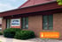 Exterior of Optima Medical General Practice, a brick building with red siding and green bushes.
