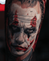 Detailreiches Porträt-Tattoo des Jokers mit weißem Make-up, dunklen Augenringen und roter Clownsmaskierung.