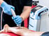 A practitioner in blue gloves applies a shockwave therapy device to a patient's calf muscle in a clinical setting.